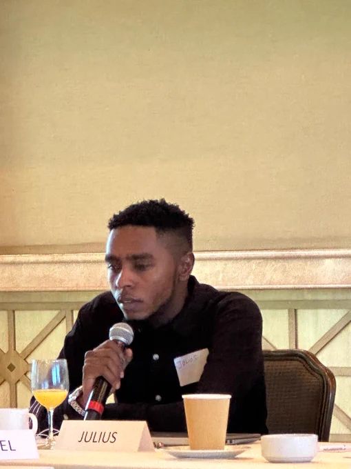 A picture of Julius Mbura holding a microphone and speaking during the AT Scale ideation workshop.