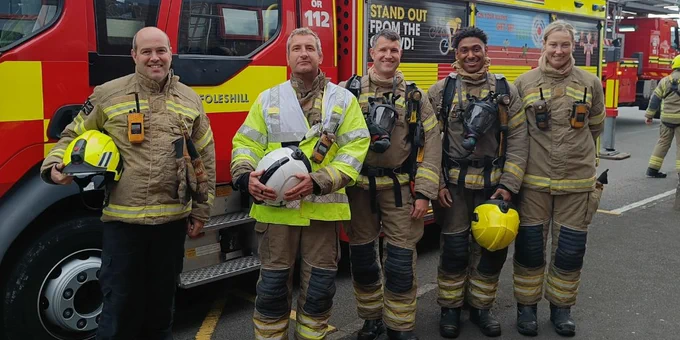 Five firefighters in fire kit stand beside a fire engine with the fire station name 'Foleshill' on the door