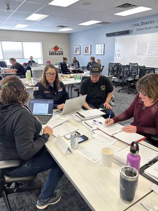 Three women and a man working around a table with binders and laptops open talking through an emergency scenario.