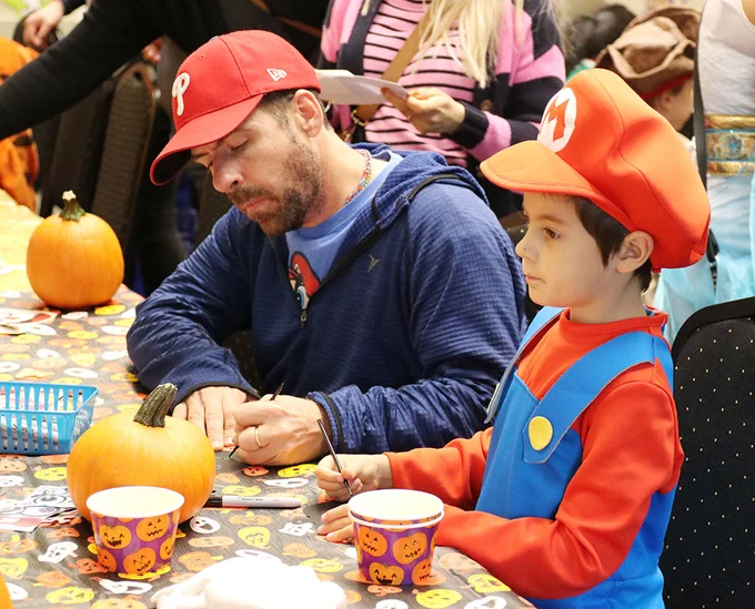 A man and a boy decorate pumpkins at a craft table.