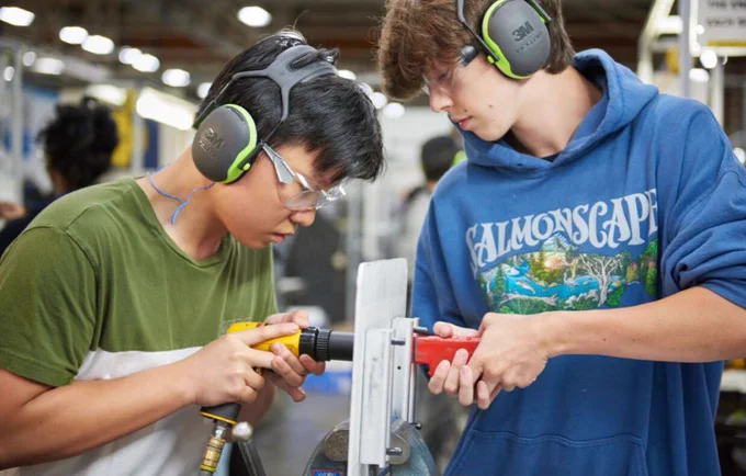 Two students working on a hands-on project using tools inside of a factory. 