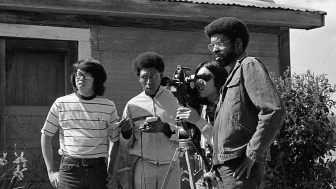 Four student filmmakers standing next to a movie camera.