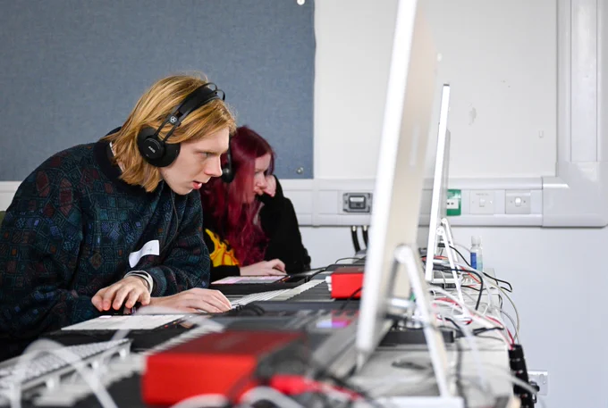 Two students wearing headphones whilst working at computers.
