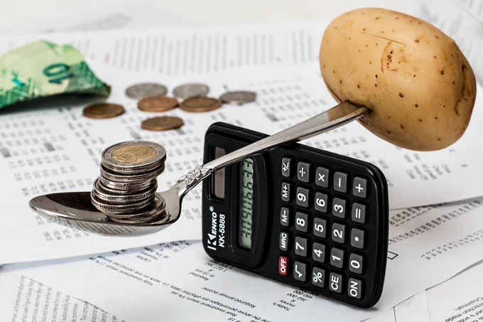 A potato and coins on a spoon balanced over a calculator