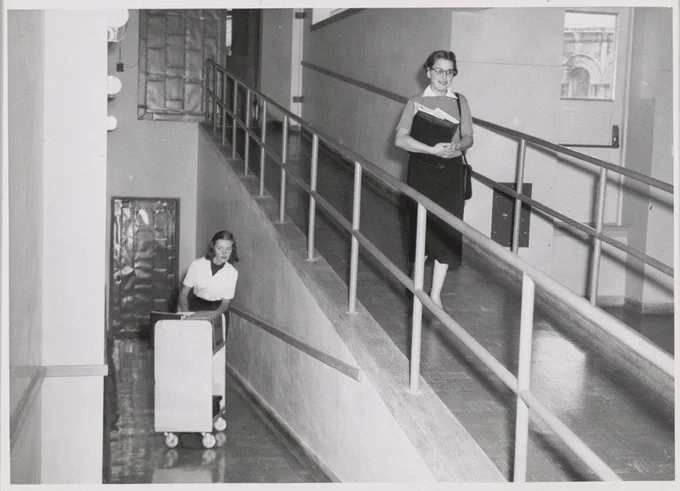 Library staff members, one pushing a library cart, one holding documents.