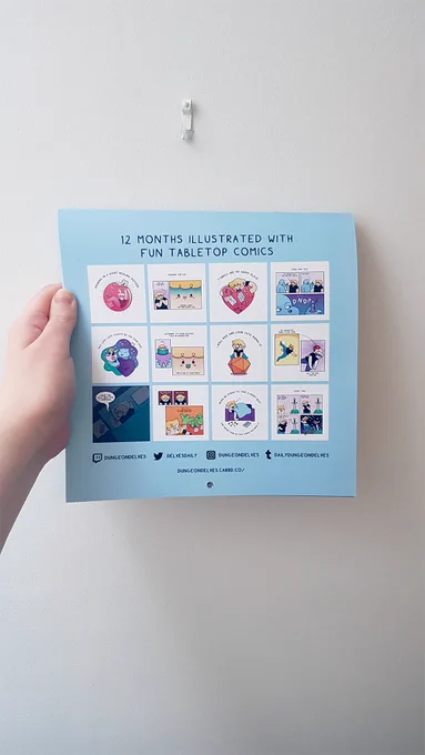 "12 months illustrated with fun tabletop comics."

Image of a hand holding up a calendar against a white wall. The back of the calendar shows the 12 images inside.