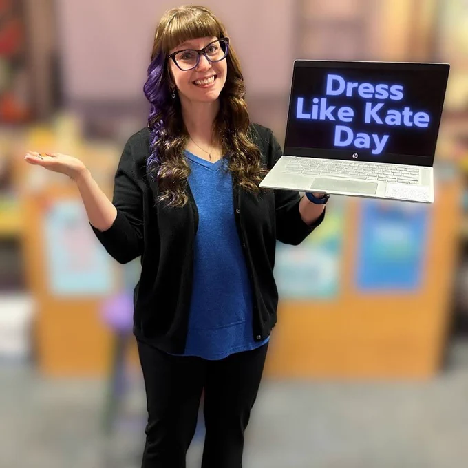 Mrs. Karpiuk holding a Chromebook with the words Dress Like Kate Day