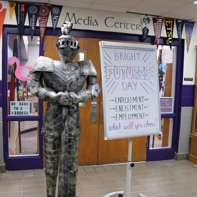 A metal knight outside of the media center with a sign that says "Bright futures day. Enrollment, enlistment, employment. Which will you choose?"