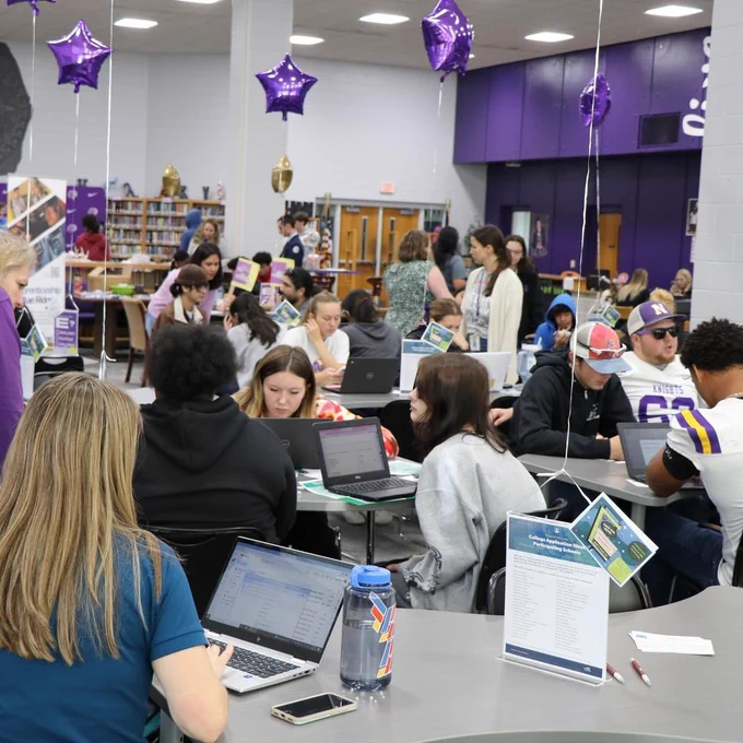 The media center filled with about 20 students at tables with their computers receiving help from adults.