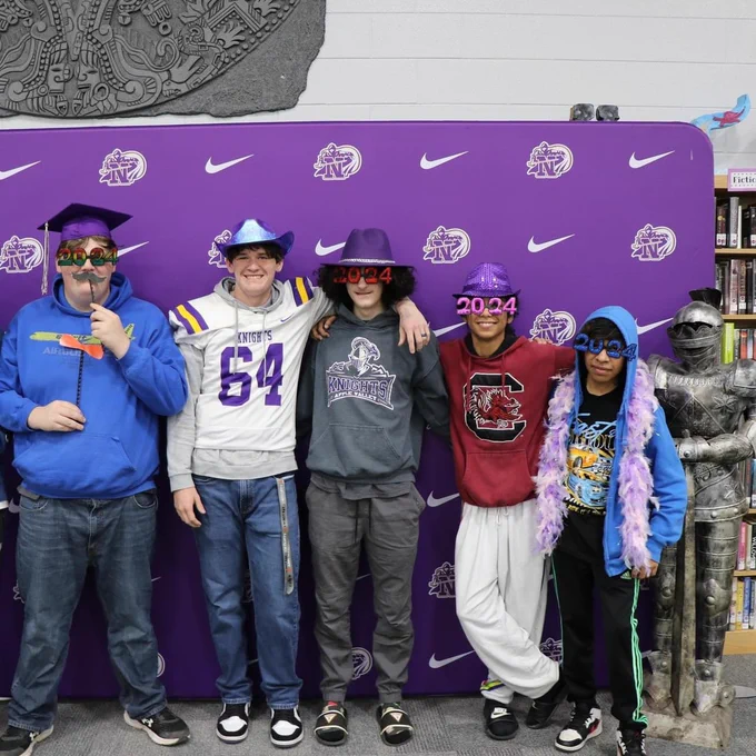 A group photo of five students in front of a North backdrop. The students are using photo props like 2024 glasses, caps, and other items.