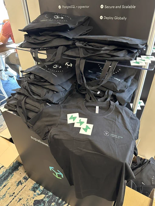 tshirts and totes sprayed around a conference booth with the title supabase vector 