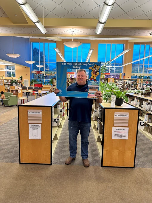 Man holding a sign that reads "I got my first library card today!"