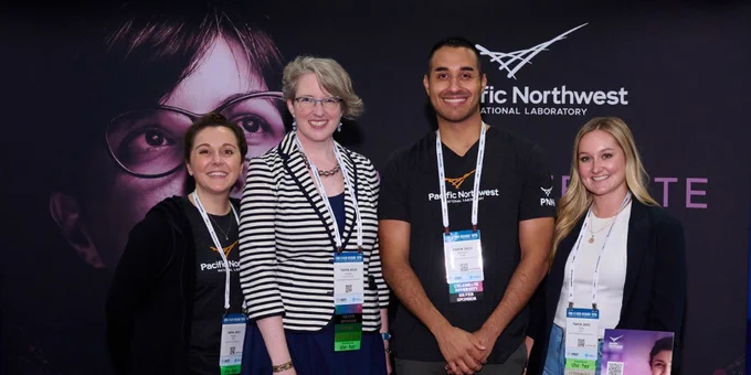 PNNL staff members smiling at the camera from behind a recruitment booth
