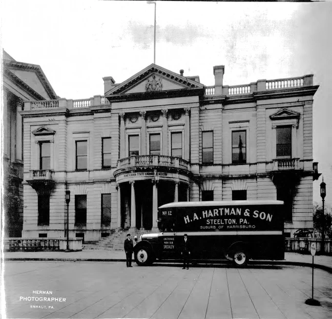 A H.A. Hartman & Sons truck and two individuals stand outside of a government building. 