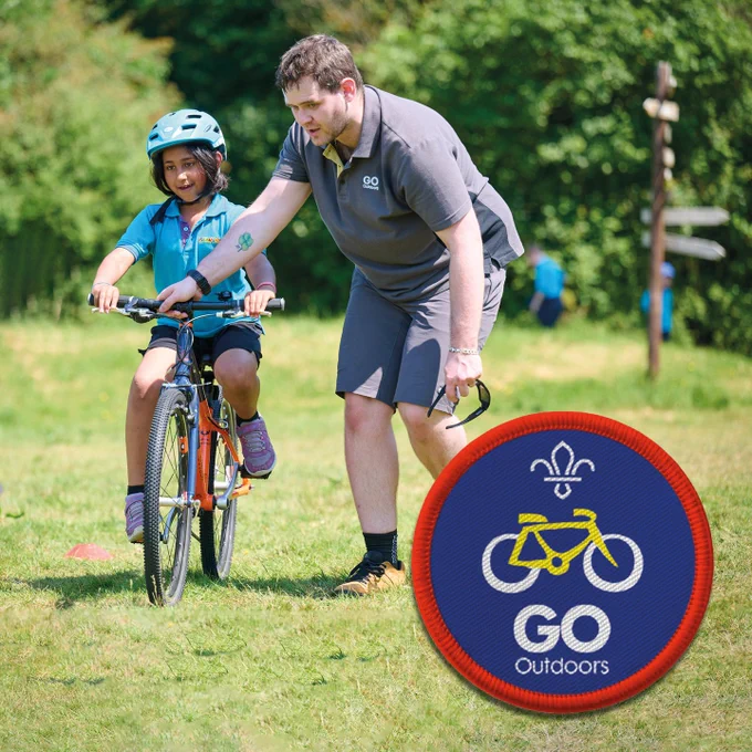 A young person wearing bright blue cycling with the help of an adult in grey.