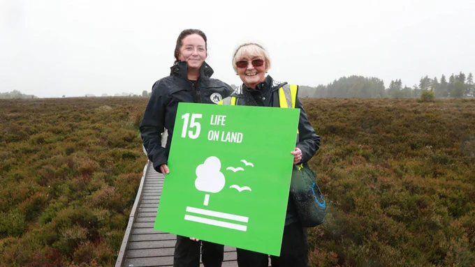 Two people standing on a wooden walkway, holding up a sign that reads ’15 – Life on Land’