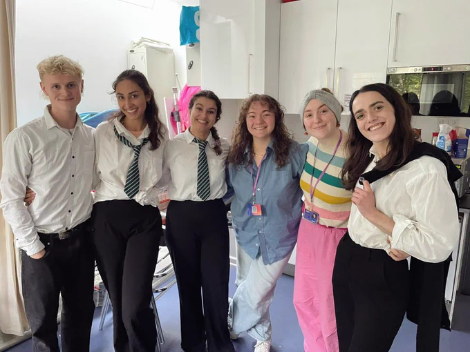 A post show photo with four actors in school uniform standing backstage with the two writers of the show 