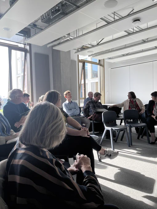 Group of people in a room talking some people turned to the back left of the photo to someone talking