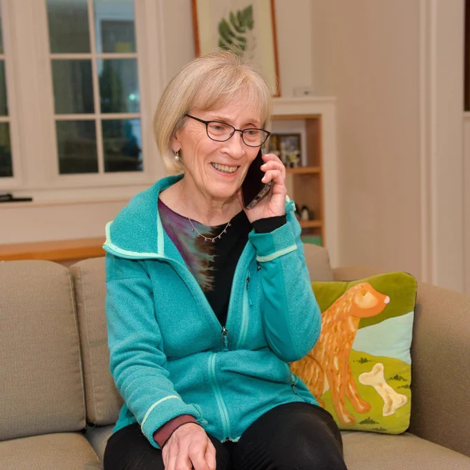Claudia Goldin talks on a cell phone while sitting on a couch in her home