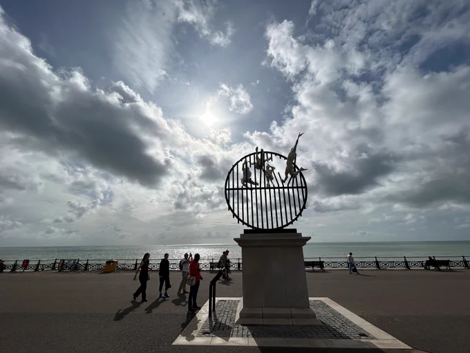 Sculpture on Hove plinth with the sea in the background with Sun appearing through the clouds