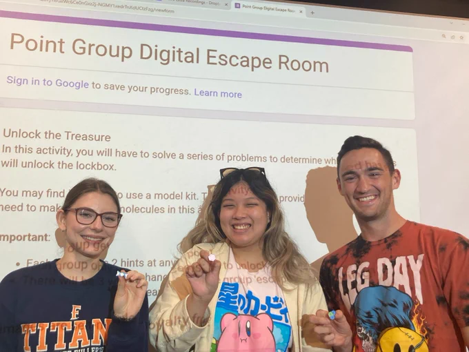 Photo of three students in front of a projector screen (Team Particle In A Box)