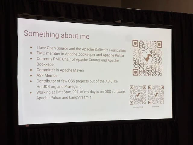 Photo of a projected conference slide, discussing "Something About me", introducing the speaker and their background. On the right side of the slide, are three separate QR codes linking to the speaker's websites or background - and each QR code has the Mozilla dinosaur in the middle. Very cute - and useful.