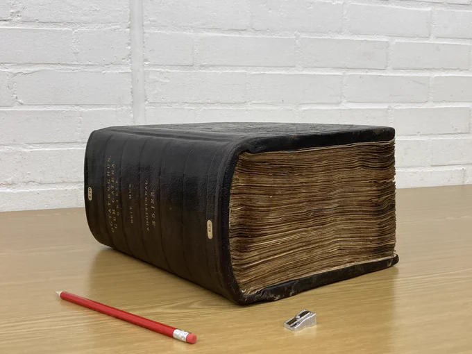 An enormous manuscript of the Greek Octateuch, positioned on a table beside a pencil and pencil sharpener to indicate the scale. 