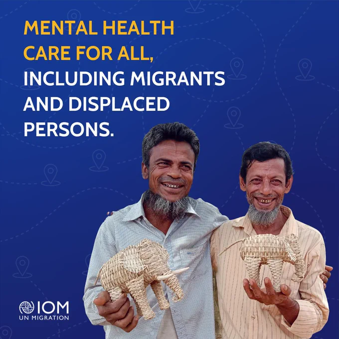 Two men, standing and smiling, holding a pair of handmade woven elephants. The text reads "Mental health care for all, including migrants and displaced persons." 