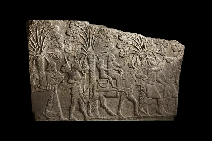 Fragment of a stone relief depicting a procession of figures and animals, with palm trees behind. It comes from Ninevah and dates to around 700 BCE.