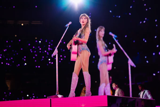 A woman (Taylor Swft) on stage with a guitar and mic 