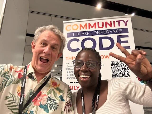 Photo of two happy conference goers in front of the Community Over Code banner - smiles all around!