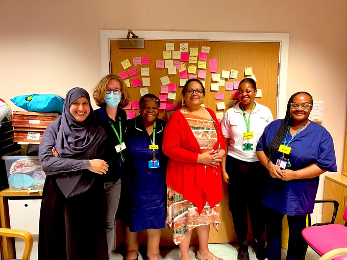 Photo of 6 people smiling in front of a wall covered in post it notes