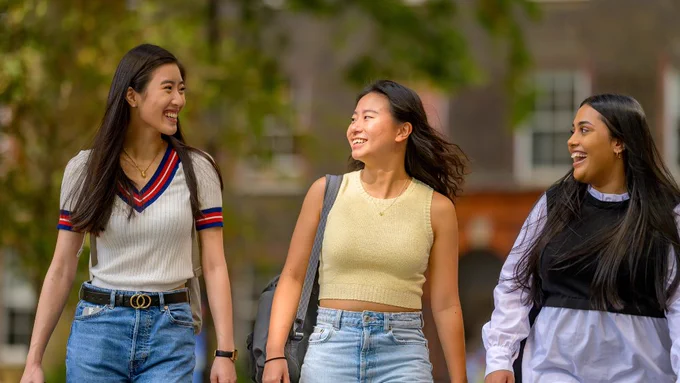 Three smiling students talking to each other as they walk through the quad at Guy's campus. Visible, out of focus, in the background is part of a building at the quad.