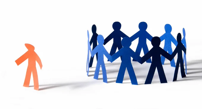 A group of blue papercut people holding hands in a circle with a red papercut person on the side-lines. 