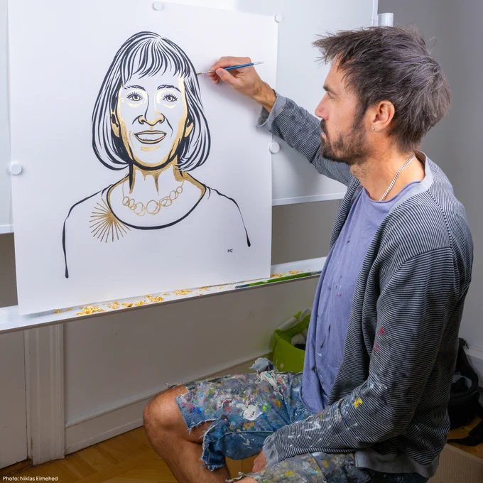 An image of Niklas Elmehed putting the finishing touches on the illustrations of the chemistry laureates. He is working on Claudia Goldin's portrait. He is dressed casually.