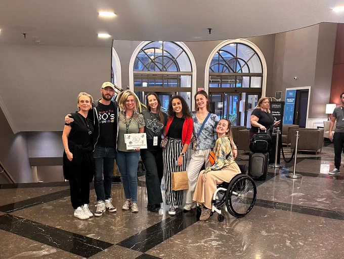 Group photo in the hotel hall. Seven people from the Candoco and Fall for Dance North team are next to each other, posing for the picture. One person in the middle is holding a sign with the Festival’s logo reading ‘Fall for Dance North’.