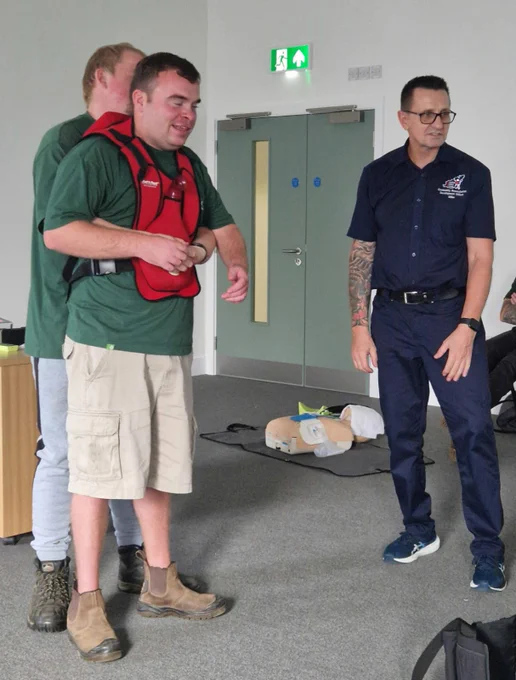 A man with a red top on being pulled from behind. Another man with cardiac support group top on taking