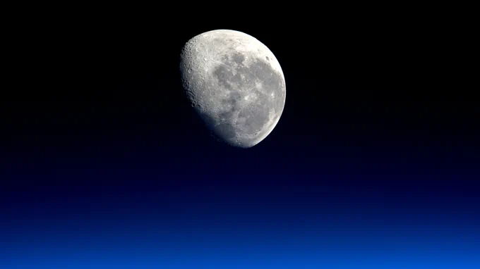 This image of the Moon was taken on March 28, 2016, by Engineer Tim Peake of the European Space Agency during Expedition 47 on the International Space Station. The Moon is partially illuminated and craters are visible on its gray surface. The sky in the background is a gradient of dark blue to black. Credit: NASA