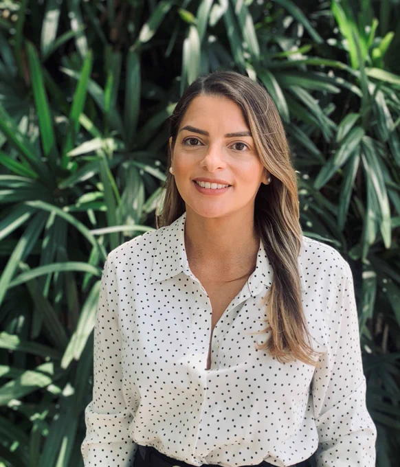 Prof. Pagán-Torres, wearing a white shirt with black spots, smiling and in front of some green foliage.