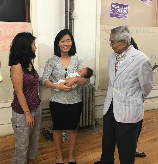 Mayor Wu holds one of her infant children in her arms while chatting with Frank Chin and another community member.
