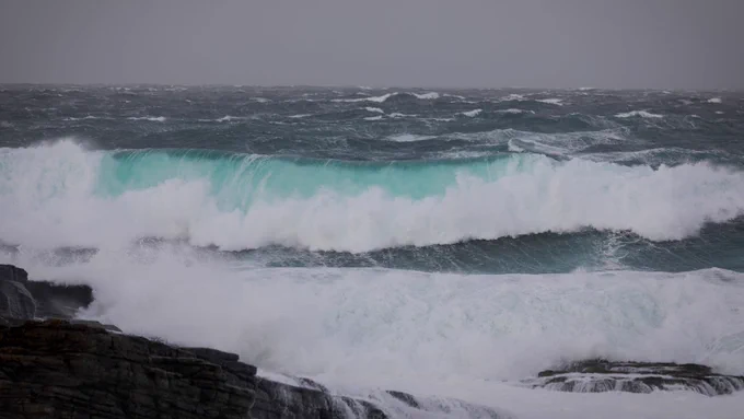 View of large, bright blue, waves rolling shore in Orkney