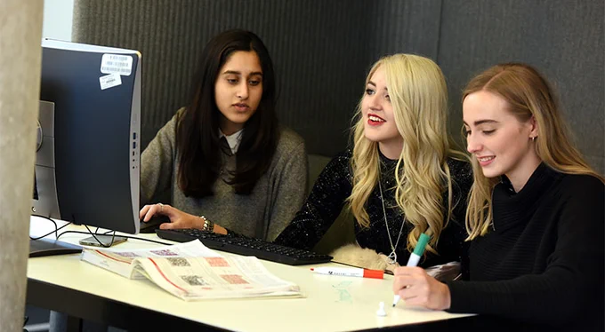 3 students are sitting behind a computer studying together
