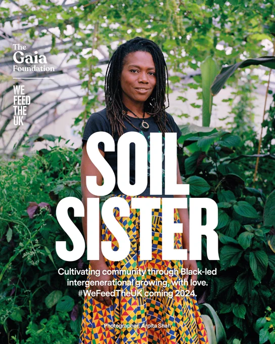 portrait of a woman standing amidst a backdrop of plant life inside a large greenhouse where the urban growing projects take place in London. She wears a black t-shirt that reads Black Rootz and a vibrant multicoloured skirt. The text reads: Soil Sister, cultivating community through Black-led intergenerational growing with love.