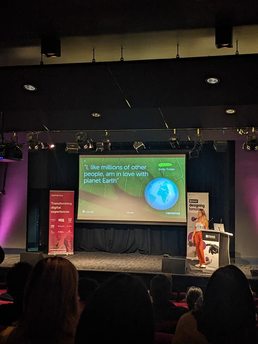 Emily on stage at Interact 2023. Screen reads 'I, like millions of other people, am in love with planet earth' 