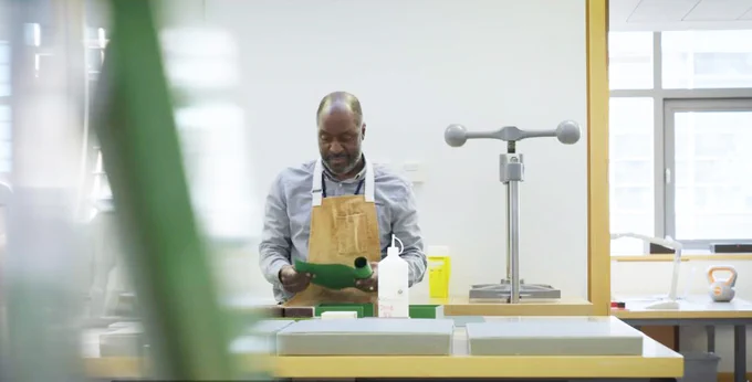Our conservator, Roger, stands at a desk wearing an apron, rolling out a piece of green paper. Other bottles and cans rest on the desk next to him.
