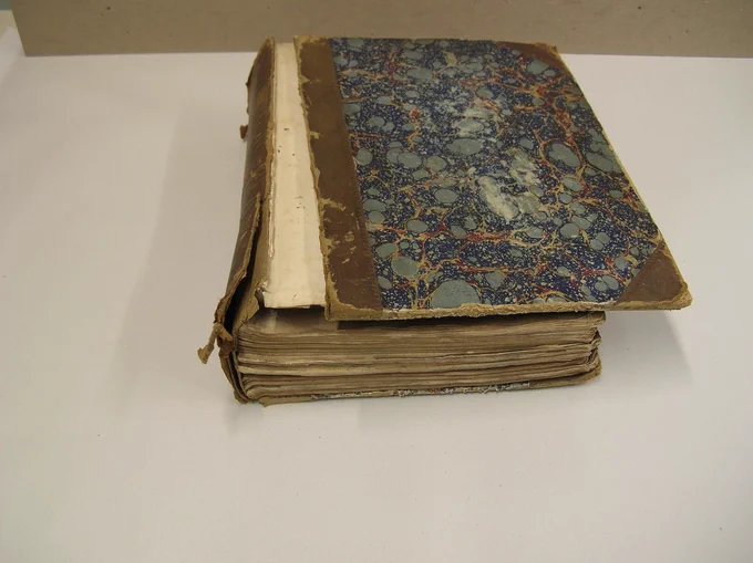 A large bound book lays tattered on a desk, its front cover split from the spine.