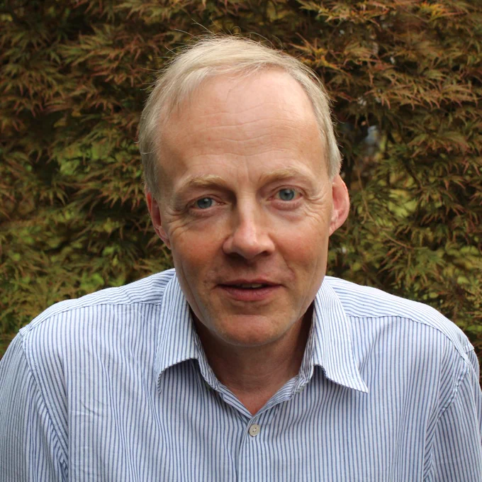 Hugh in a striped blue shirt standing outside. He has short grey hair and blue eyes. 