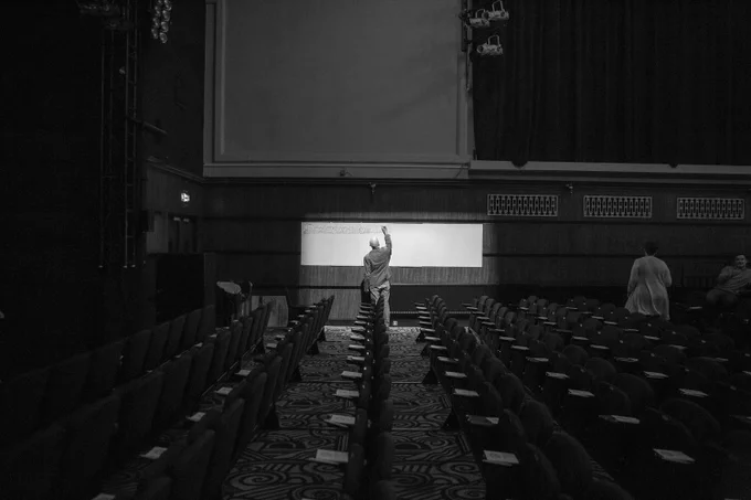 An empty theatre auditorium, with a cartoonist doodling on white boards along the side wall.