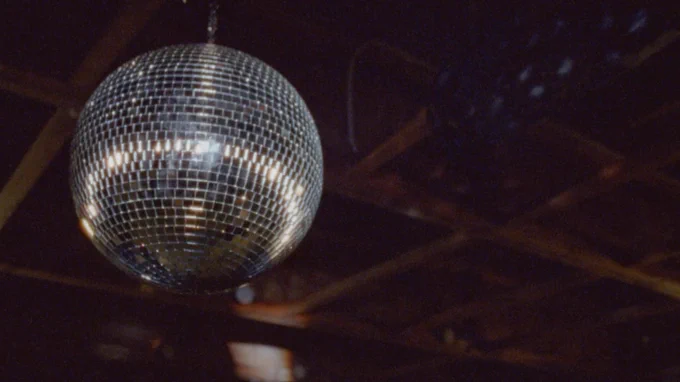 A disco ball hung from wooden beams spins and reflects the light. 