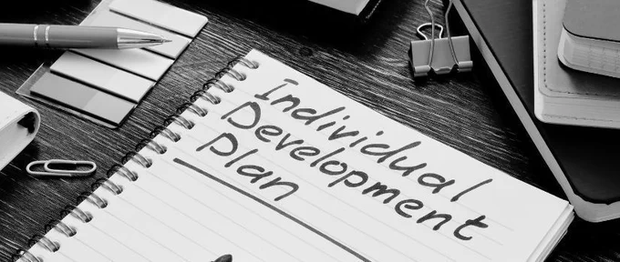 top of desk with pen, notebooks, paperclips, Open spiral notebook with "Individual Development Plan" written on the page